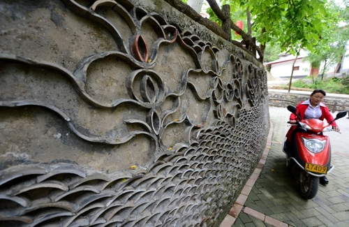 5月27日，在甘肃省陇南市康县王坝乡大水沟村，一名村民驾车从用废旧瓦片装饰的花坛旁走过。