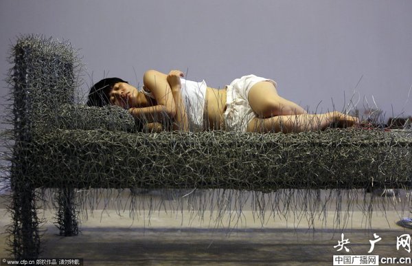 2014年8月11日，北京，中国女艺术家周洁在北京现在画廊的展厅睡在一个未完成的铁丝床上，这一艺术项目被命名为“36天”，而这36天里，她可以正常进食、洗漱、如厕，以及玩手机等。