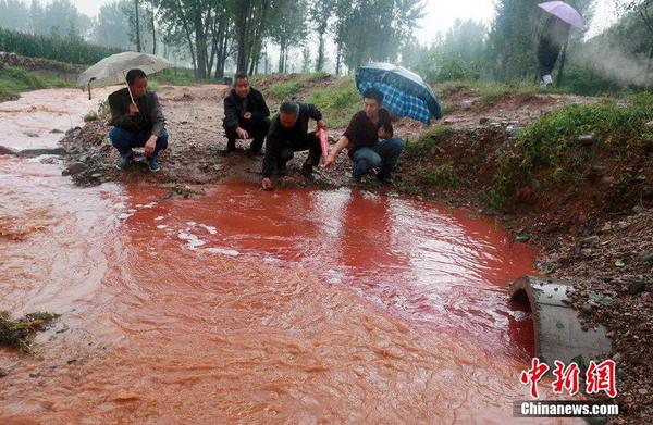 2014年9月15日，河南洛阳汝阳县马兰河因为污染变成一条“红河”，“红水”顺着山坡一直流到山下，而“红水”的源头正是附近一山顶的染料厂残留处理池。图为管道里冒出的红色污水与山上流下的雨水泾渭分明地流入马兰河。