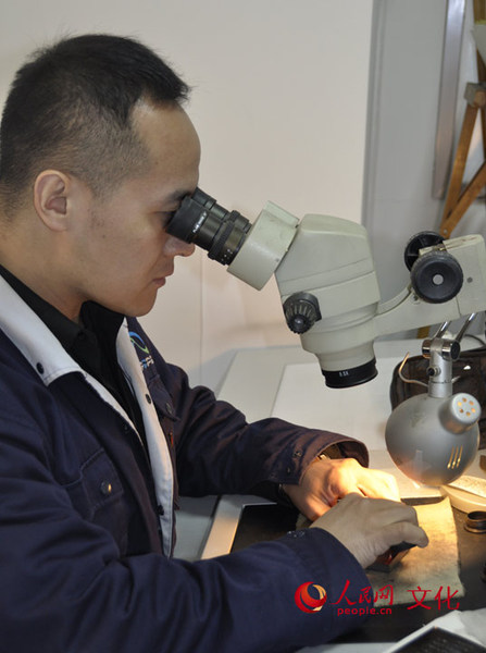 雕刻师正通过高倍放大镜，手持刀具在一块小小的钢版上，用手工雕刻出与邮票票面同样大小的部分图案。（人民网 王鹤瑾 摄）