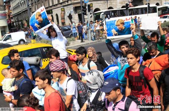 资料图：难民们手持默克尔的照片，从匈牙利步行前往奥地利。