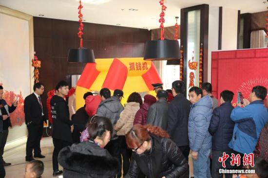 资料图：2016年2月27日，山东东营，看房的市民在商家设置的“抢钱机”内抢着飞舞的人民币，抢到的人民币归市民所有。由于房地产市场低迷，山东东营的某楼盘为了吸引前来看房的市民，在售楼处安装了“抢钱机”，看房的市民排成长队“抢钱”，用真金白银刺激看房客。 图片来源：视觉中国