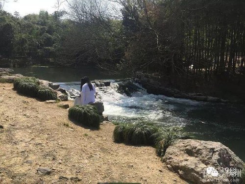 图为一白衣长发人坐水边抚琴。