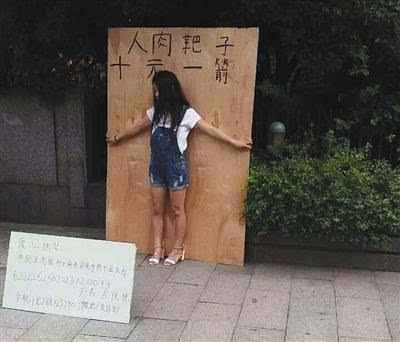 　杭州武林广场一女孩站在一块大木板前头，木板上写有“人肉靶子，十元一箭”字样。