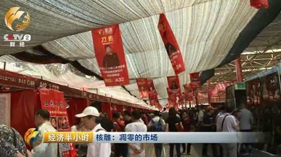 潘家园旧货市场的这块空地上，临时支起了一些棚子和摊位，正在举办一个核雕展销会。顶棚上方高高悬挂着前来参加展销会的雕刻师的照片。