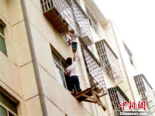 一业主左手抓住窗户边沿，右手托举男孩双脚 宋俊初 摄