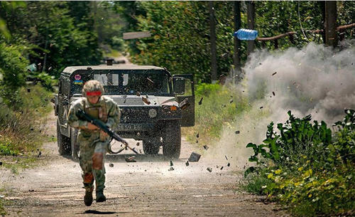 图为乌政府军的悍马军车遭到伏击，附近发生爆炸，沙石乱溅，一只塑料瓶凌空飞起，一名乌军士兵在前方躲避敌方火力。