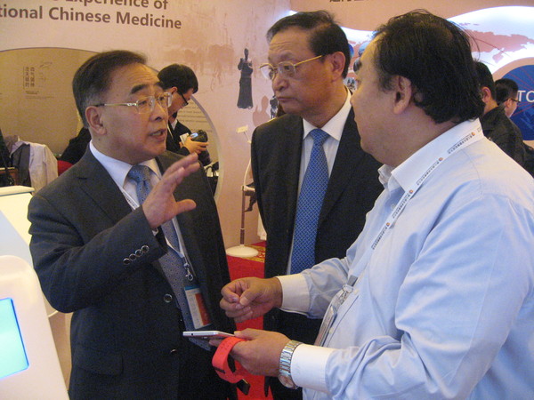 二、王国强（中）与中国中医科学院院长、中国工程院院士张伯礼（左一）在第九届全球健康促进大会中医药体验展馆尚力博士的导引下参观。 人民政协网记者 张春莉 摄影