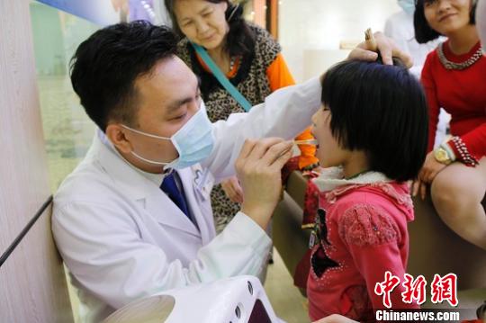 张菲(左2)看着孩子接受免费的口腔检查?！⌒そ?摄