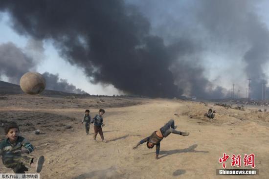 苦中作乐是孩子们的宝贵技能，大人们会逐渐被现实的痛苦和窘境压倒，失去追求快乐的能力，但孩子们不会。他们永远能在艰苦的条件下获得快乐，因为他们追求的快乐非常简单。图为当地时间2016年11月23日，伊拉克摩苏尔，极端分子在逃离Al Qayyarah小镇前点燃油井，几名儿童在滚滚浓烟中踢球。