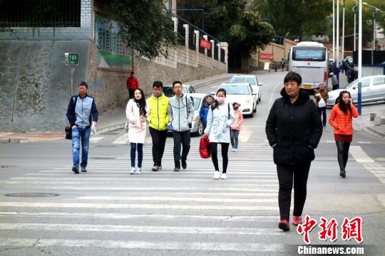 图为市民们穿着棉服、羽绒服在寒风中卷缩着过马路?！∷镱?摄