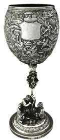 征战图高脚杯   Standing Trophy with Battle Scene Pattern 晚清 通高：29cm；口径：9.5cm；底径：10.6cm；重:681g 款识：慎昌，LW   清代中晚期，随着外销银器的逐渐升温，银匠不仅开始借鉴青铜器、瓷器的特征创造银器，更融合进宗教思想及丰富的想象力。征战图高脚杯的杯身运用锤揲工艺由内向外敲击出隋唐故事“罗通扫北”浮雕图，在杯身中央位置留有一醒目光面盾牌，用以錾刻购买者家族族徽，一方面彰显其身份地位，另一方面也能够起到防盗的作用。整体造型极具艺术感，杯托被设计成一只展翅翱翔的雄鹰，杯杆被设计成配有圆环的锡杖造型。底座焊接一打坐罗汉和一伏虎抱杵罗汉，底座整体设计成须弥山的造型，须弥山在印度佛教中象征着世界之中心，整体做工精湛，布局巧妙，体现了银匠的艺术造诣与佛教思想的融合。