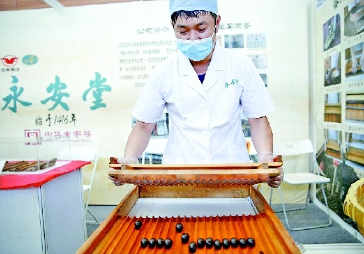 ▲图为工作人员在活动现场向观众展示中药蜜丸制作工艺。