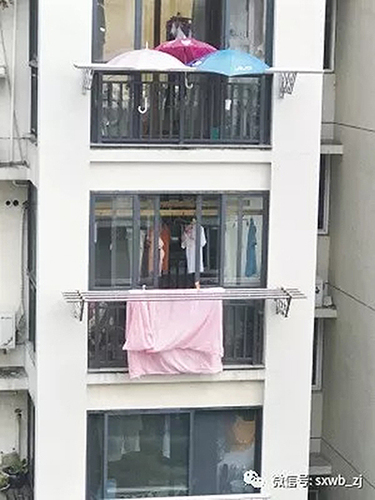 下雨了楼下被子还晒在外面:楼上住户在阳台撑3把伞