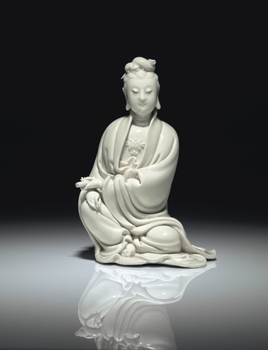 明十七世纪初 德化白釉书卷观音坐像 《何朝宗》葫芦形印款，高8 58 寸 (21.9公分)。估价：60,000-80,000美元。此拍品于2018年9月13至14日在佳士得纽约亚洲艺术周之中国瓷器及工艺精品拍卖中呈献。