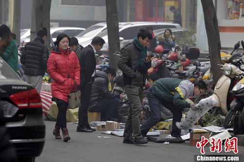 一家快递公司的员工蹲在马路边分发邮件，身边堆放着大量的包裹。 王中举 摄 