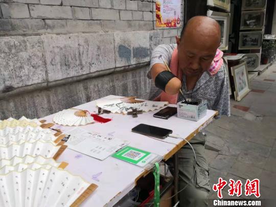 贾维军坐在自己的简易摊位前写字?！“⒘漳?摄