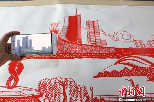 图为丁健对比照片与剪纸作品。　夏莹 摄